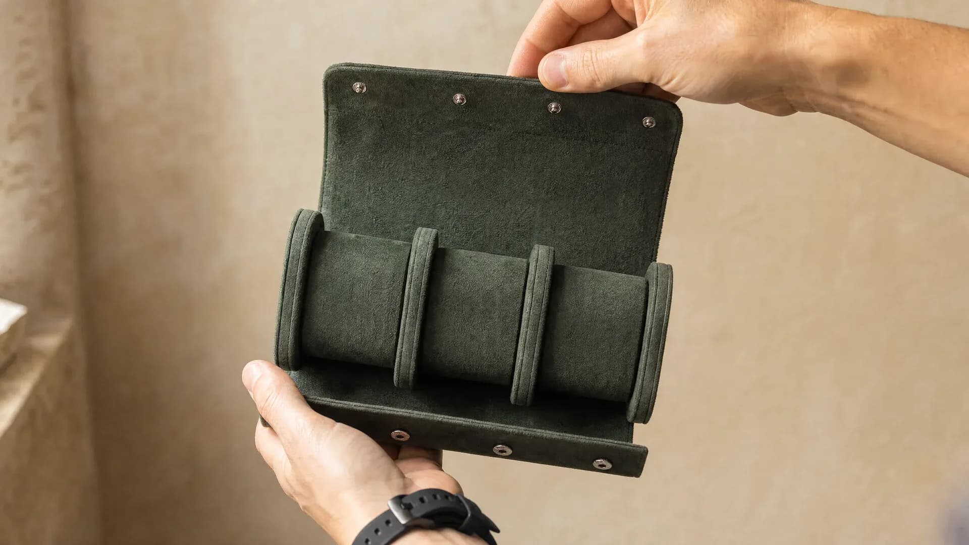 Manos sosteniendo un estuche verde abierto con espacio para tres relojes
